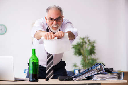 Old male employee drinking alcohol in the officeの写真素材