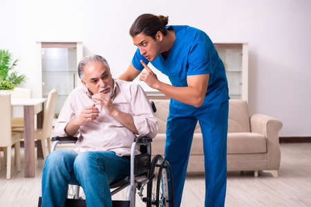 Old man in wheel-chair and young bad caregiver indoorsの写真素材