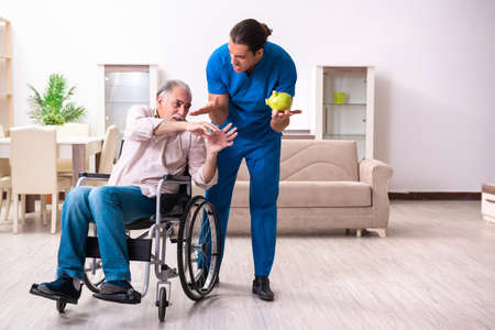 Old man in wheel-chair and young bad caregiver indoorsの写真素材