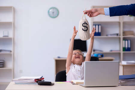Funny small girl receiving salary in the officeの写真素材