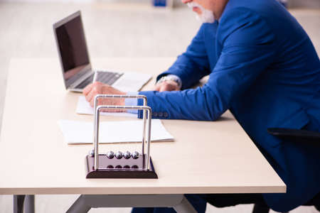 Old male employee businessman and meditation balls on the desk
