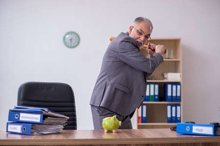 Old male employee holding baseball bat in budget planning concepの写真素材