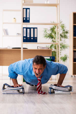 Young male employee doing sport exercises at workplaceの写真素材