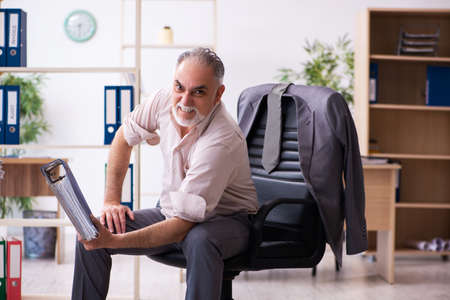 Old male employee doing physical exercises at workplaceの写真素材
