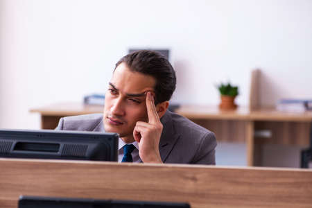 Young male employee unhappy with excessive work in the officeの写真素材