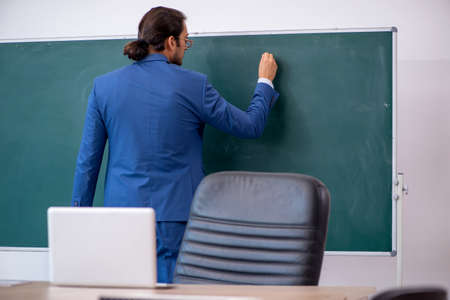 Young male teacher in suit in front of green boardの写真素材