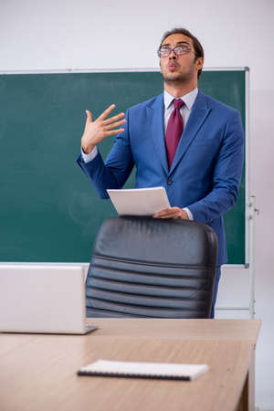 Young male teacher in suit in front of green boardの写真素材