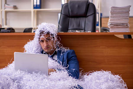 Young male employee and a lot of cut papers in the officeの写真素材