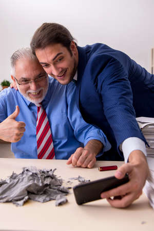 Young male employee and old boss burning papers at workplaceの写真素材