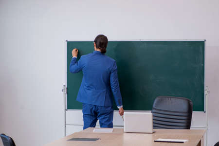 Young male teacher in suit in front of green boardの写真素材