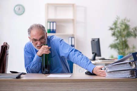 Old male employee drinking alcohol in the officeの写真素材