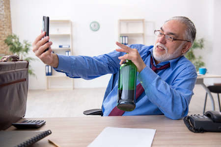 Old male employee drinking alcohol in the officeの写真素材
