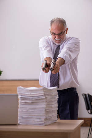 Old male employee holding gun unhappy with excessive workの写真素材