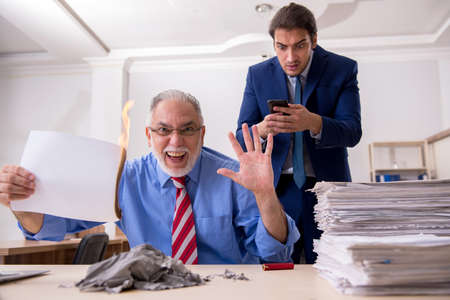 Young male employee and old boss burning papers at workplace