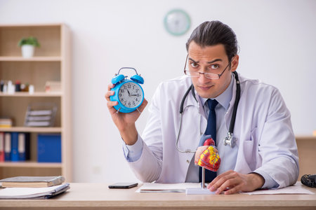 Young male doctor cardiologist in time management conceptの写真素材