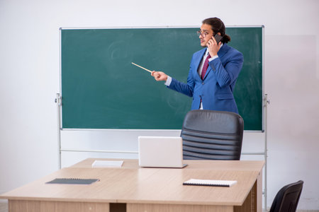 Young male teacher in suit in front of green boardの写真素材