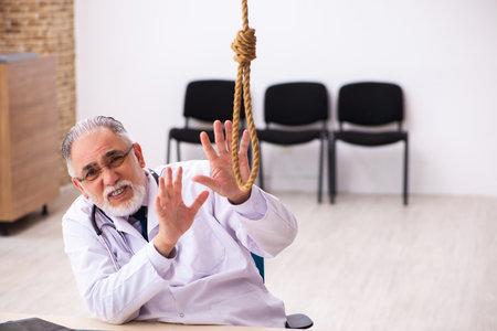Old male doctor committing suicide at workplaceの写真素材