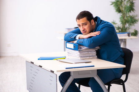 Young male employee unhappy with excessive work in the officeの写真素材