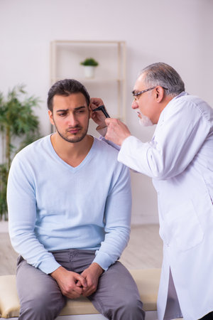Young sick man visiting old doctor otolaryngologistの写真素材