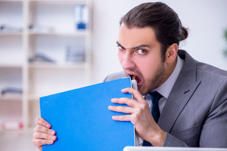 Young male employee unhappy with excessive work in the officeの写真素材