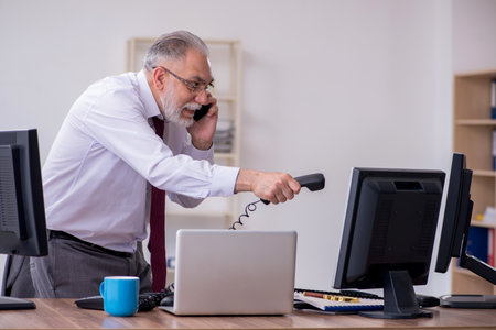 Old male boss sitting at desktop in the officeの写真素材