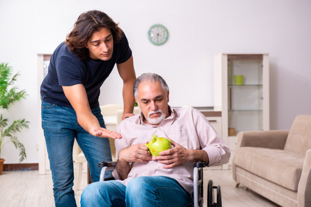Old man in wheel-chair and young bad caregiver indoorsの写真素材