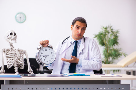 Young male doctor and skeleton patient in time management concepの写真素材