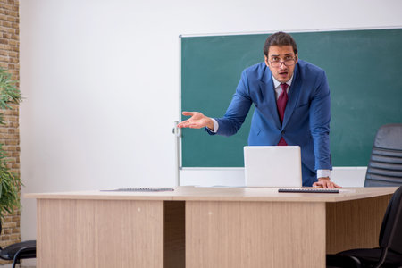 Young male teacher in suit in front of green boardの写真素材