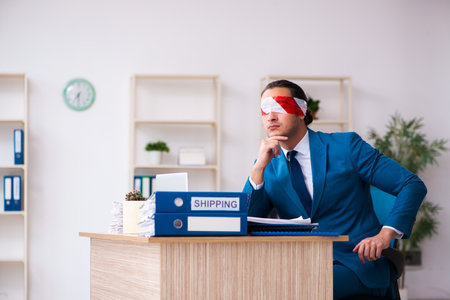 Blindfolded male employee working in the officeの写真素材