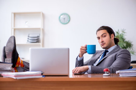 Young male employee drinking coffee in the officeの写真素材