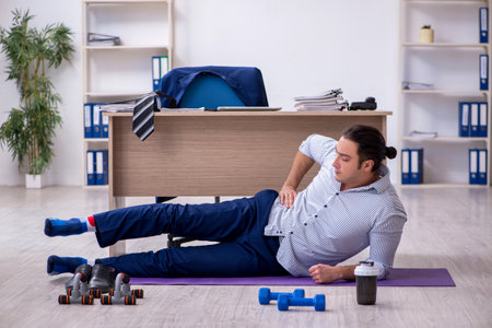 Young handsome male employee doing exercises in the officeの写真素材