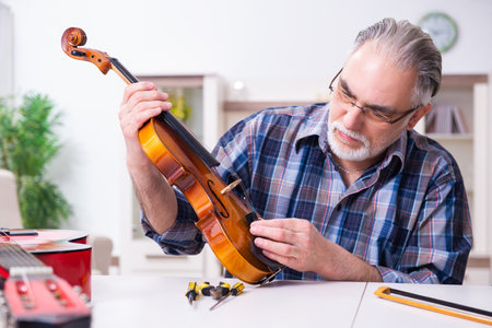 Senior male repairman repairing musical instruments at homeの写真素材