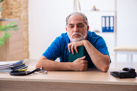 Old male doctor extremely tired after night shiftの写真素材