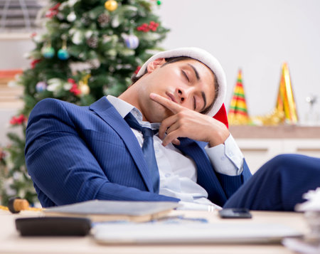 Young handsome employee celebrating Christmas at workplaceの写真素材