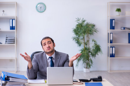 Young male employee unhappy with excessive work in the officeの写真素材