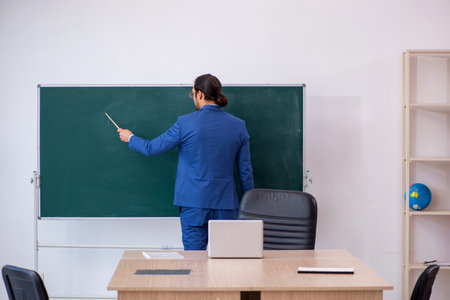 Young male teacher in suit in front of green boardの写真素材