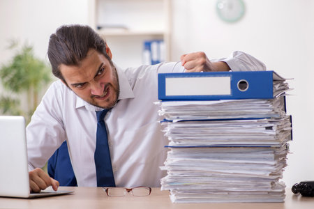 Young businessman unhappy with excessive work in the officeの写真素材
