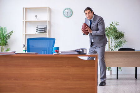 Young male employee with rugby ball in the officeの写真素材