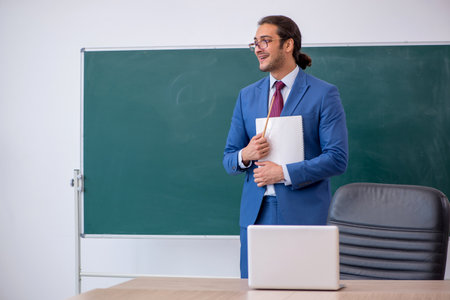 Young male teacher in suit in front of green boardの写真素材