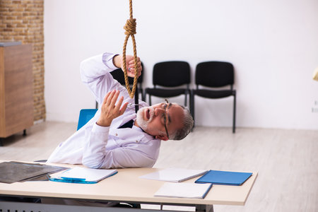 Old male doctor committing suicide at workplaceの写真素材