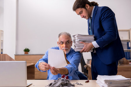 Young male employee and old boss burning papers at workplaceの写真素材