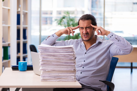 Young male employee unhappy with excessive work in the officeの写真素材