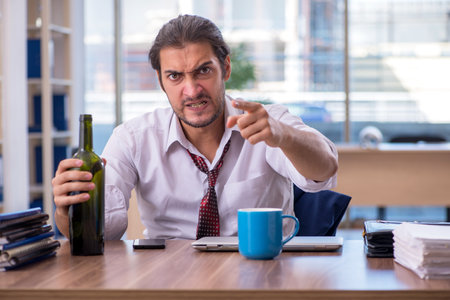 Young male alcohol addicted employee working in the officeの写真素材