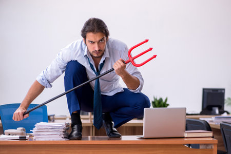 Young devil businessman holding trident in the officeの写真素材