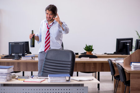 Young male employee drinking alcohol in the officeの写真素材