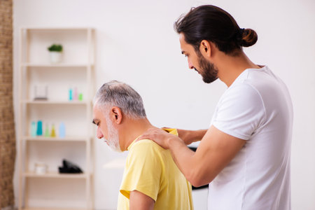 Old male patient visiting young male doctor chiropractorの写真素材