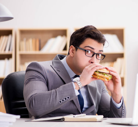 Hungry funny businessman eating junk food sandwichの写真素材