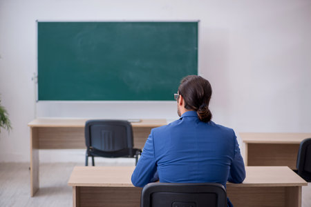 Young male teacher in suit in front of green boardの写真素材