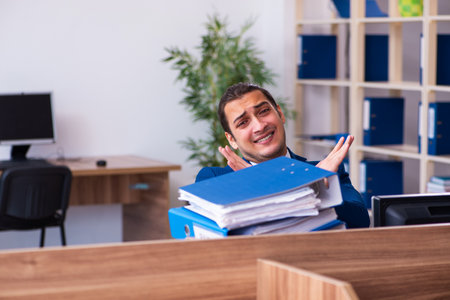 Young male employee unhappy with excessive work in the officeの写真素材