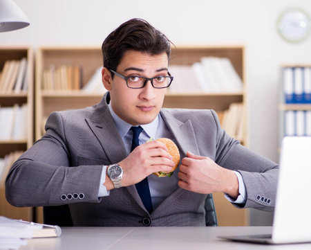 Hungry funny businessman eating junk food sandwichの写真素材